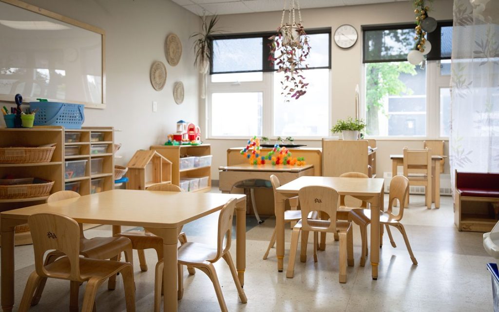 Salle de jeux. Des tables et des chaises en bois sont disposées au centre de la pièce