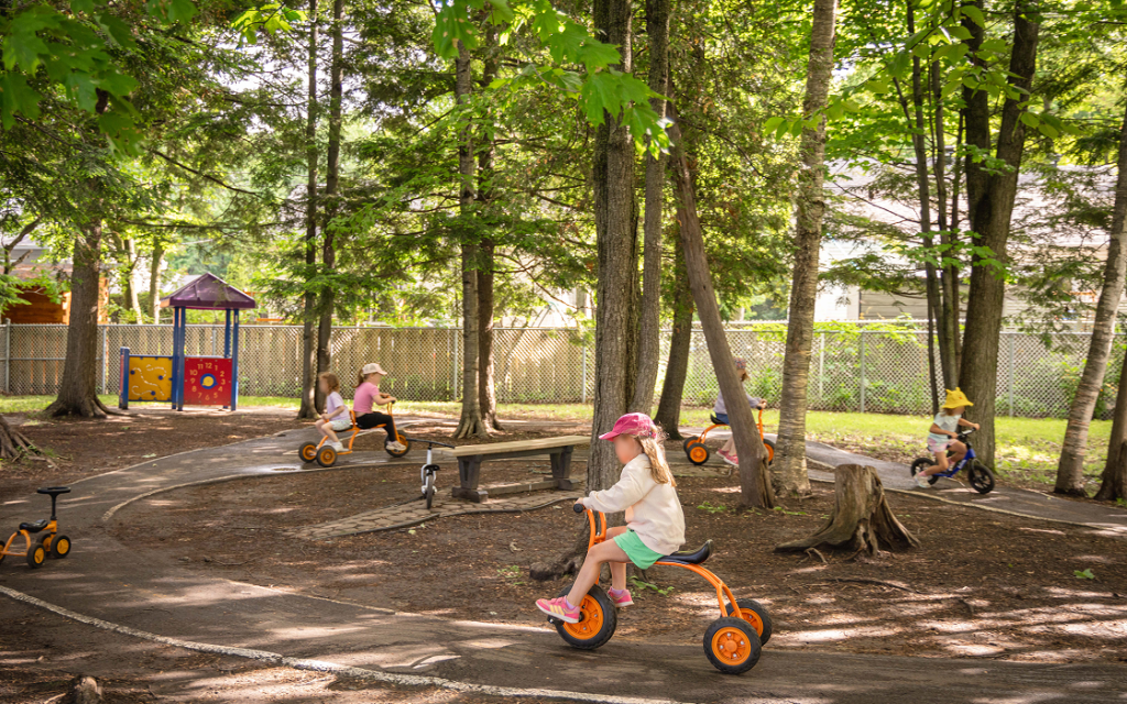 Des enfants font du tricycle sur une piste dans un boisé