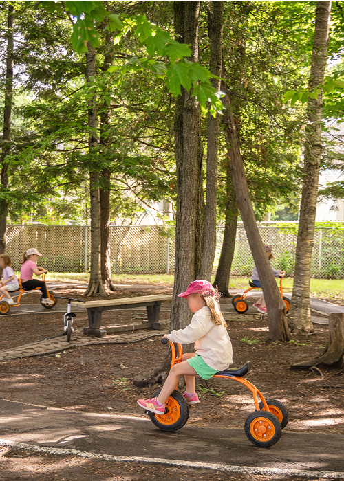 Des enfants font du tricycle sur une piste dans un boisé